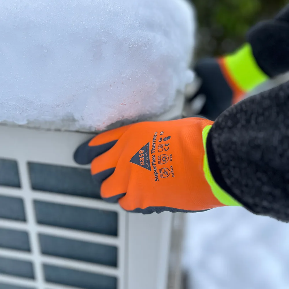 Orangefarbener HASE Kältehandschuh SuperFlex Thermo+ auf einer verschneiten Außeneinheit