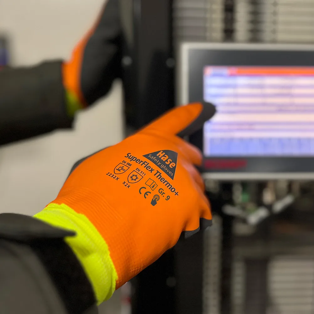 Orangefarbener HASE Kältehandschuh SuperFlex Thermo+ bedient ein Touchdisplay an einer Maschine